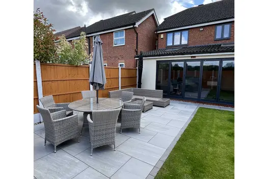 Two sets of light rattan furniture sits on Kandla Grey Porcelain Paving, back porch with french doors in the distance.