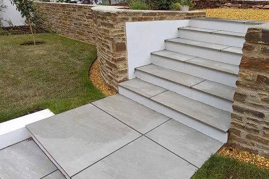 Five Kandla Grey Porcelain paving slabs as steps lead away from patio and lawn area, bordered by red brick wall.