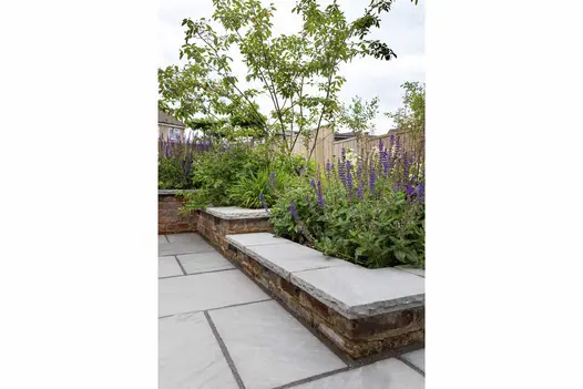 Kandla Grey Indian sandstone coping stones, with hand-cut, rock-faced edge profile, on broad brick walls retaining flower beds.