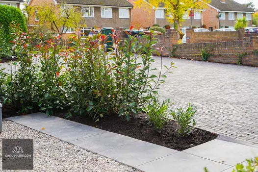 Midnight black limestone paving divides grey gravel from planted bed, next to large sloping drive, laid with clay pavers.