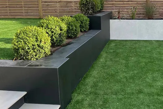 Raised walls clad with opium black designclad have topiary bushes lining the different tiers with steps in the middle.