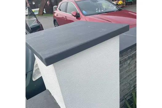 White rendered pillar topped with pier cap set into stone-clad wall capped with Brazilian Black slate coping stones.
