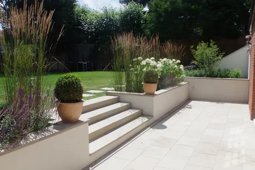 4 buff sawn sandstone steps lead from matching patio up to lawn area, rendered walls with built-in flowerbeds surround.