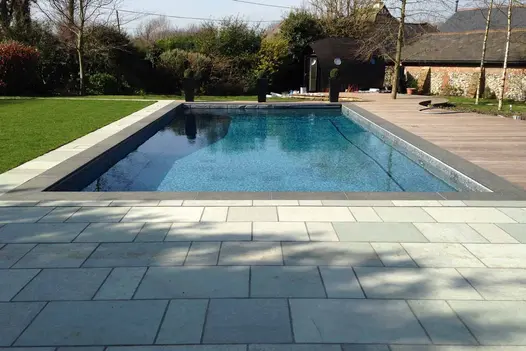 Rectangular swimming pool lined with small tiles, with lawn on 2 sides, decking and Kota Blue limestone paving on the opposite 2.
