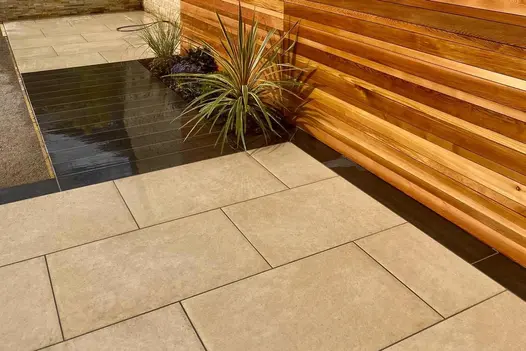 Florence beige porcelain and dark composite wood decking patio with cedarwood fence and small flower bed by Landscape By Design.