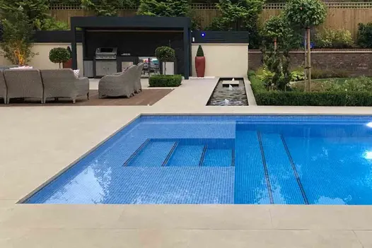 Golden Stone porcelain coping and paving surround swimming pool and rectangular pond with seating area by Landscape Design Studio.