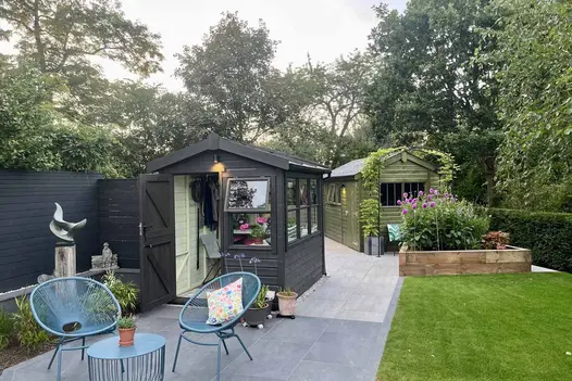 Black shed sits on travertine dark porcelain paving with blue wire furniture on kandla grey garden tiles.
