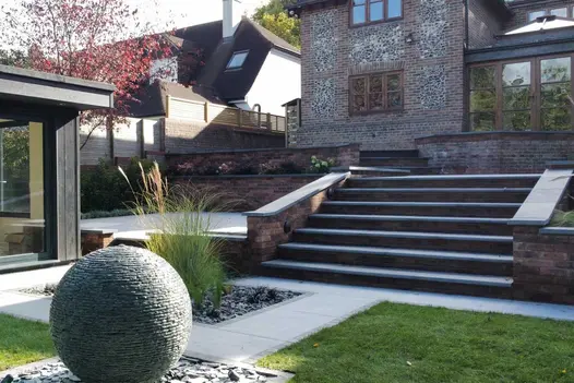 7 Brazilian Black slate bullnose steps will flank walls descend to garden with rectilinear lawn areas and spherical water feature.