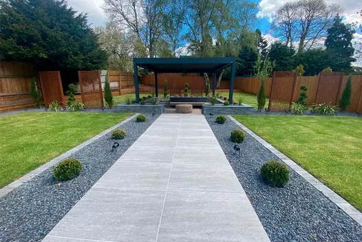 Travertine Dark porcelain path bordered with deep planted gravel beds and leading towards a pergola covered seating area.