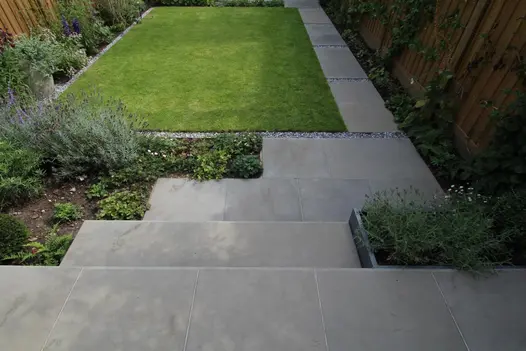 2 Heath Sawn Sandstone bullnose steps lead down to small matching pathway adjacent to well manicured lawn lined with pebbles.