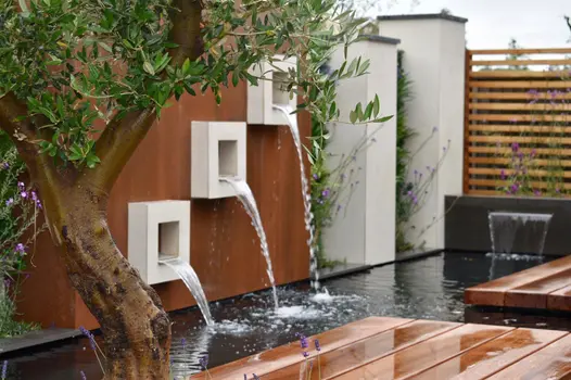 White square boxes on vintage steel premium designclad has water flowing into pond area with olive tree in foreground.
