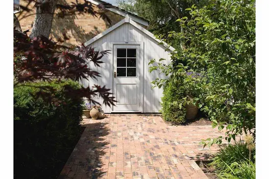 White-painted shed at junction of 2 paths of Cotswold clay pavers, laid running bond. Hedge and bushes on either side. 