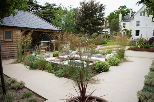 Sunken seating area in centre of Golden Stone Porcelain paving, steps up to lawn and house beyond, designed by Langdale Landscapes.