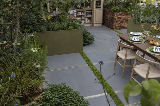 Large garden planters forming the raised borders of a cosy cottage garden paved in Sidewalk porcelain outdoor tiles.
