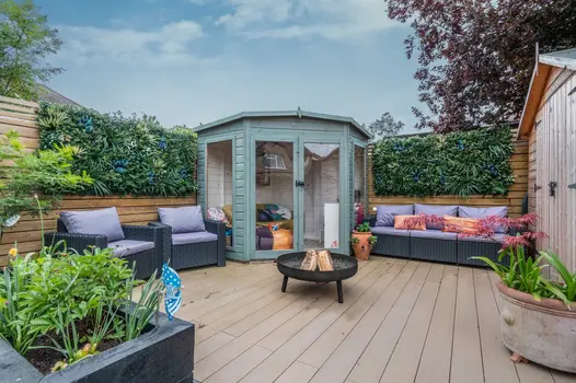 Hexagon shaped, teal coloured shed sits between rattan furniture with firepit in the middle on top of mocha designboard composite decking.