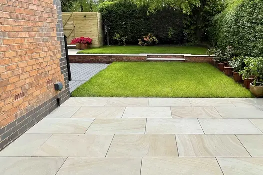 Light Buff sawn sandstone 900x600mm paving adjacent to rectangular lawn with steps up to second grass area beyond.