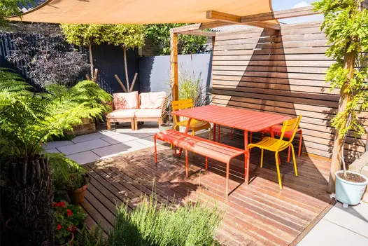 Bright orange picnic table and sunshade sits on wooden decking with light grey porcelain patio either side.