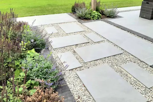 Random pattern of Light Grey Porcelain Slabs laid amongst golden gravel and edged with dark grey clay pavers.