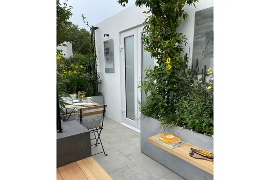 Wooden benches built into raised flower beds clad with porcelain cladding and a small garden table and chairs.