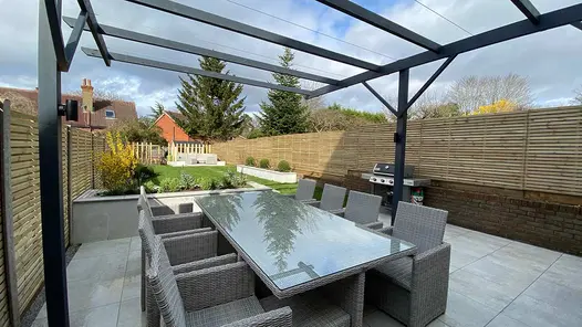 8 seater Rattan dining set on top of a Light Grey Porcelain patio and sat underneath a metal pergola feature.
