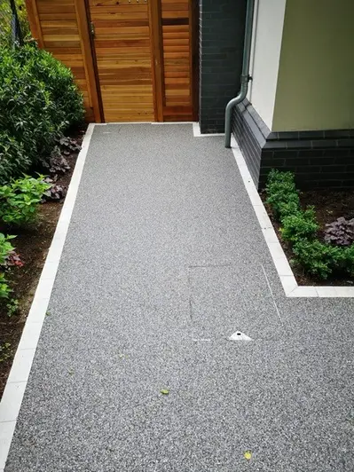 Light-grey Porcelain setts neatly edge dark-grey resin-bound gravel path by side of house between borders. Built by Landesigns Ltd.