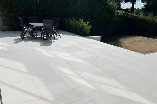 Outdoor dining area on Budget Egyptian Light Porcelain Paving, bordered by greenery. By Silveremere Landscapes.