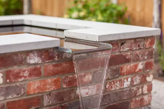 Water pours from spout of raised pond built of brick with Jura grey limestone flat coping. Design by Simon Orchard.