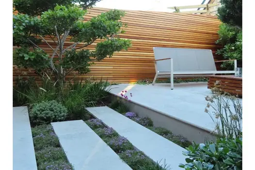 Spaced Jura grey bespoke limestone planks, thyme planted between, and bullnose-edged raised paved area with modern metal bench. 