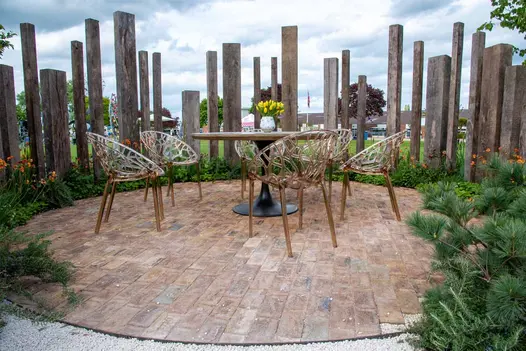 Outdoor furniture on paving circle of London Mixture Belgian Bricks, with wooden monoliths behind. Built by Landform Consultants.