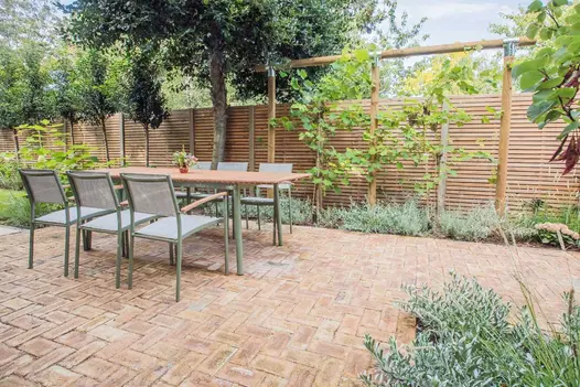 London Mixture Clay Paver Bricks used alongside wooden slatted fencing, table for 6 set upon the patio with lots of trees in the background.