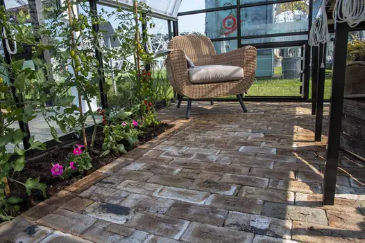 View from the ground showing London Mixture clay pavers next to flowerbed of tomato plants inside shed with rattan chair in the corner.