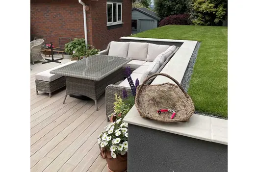 Decked patio with outdoor sofa in angle of raised lawn edged with Faro porcelain coping stones. Built by JG Landscaping.