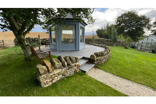 Countryside views enclosed by rock walls show circle patio of midnight black limestone with 3 bullnose steps leading up to small building.