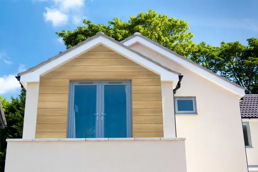 Golden Oak Millboard Shadow Line cladding used on a dormer extension, paired with cream render and grey window frames.