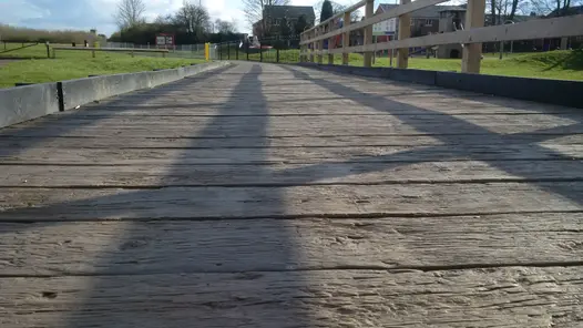 Low-level close-up of Vintage Millboard Decking near a children's park, showing the chunky profile and durability of the weathered wood design.