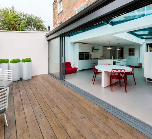 View from small deck patio using vintage millboard decking with huge french doors leading inside the traditional come modern house to kitchen.