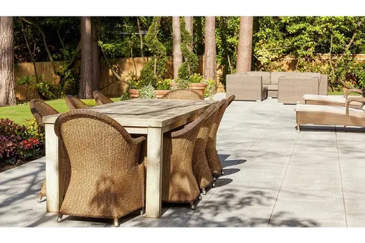 Fenced garden with lawn and tall mature tree trunks next to large patio of Silver Grey granite paving with outdoor furniture.