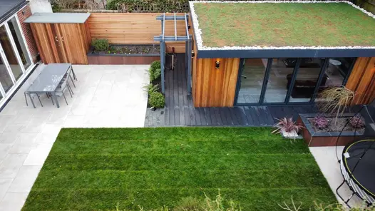 Garden office with a decking path around the outside and adjoining to a lightly coloured porcelain patio and lawn area.
