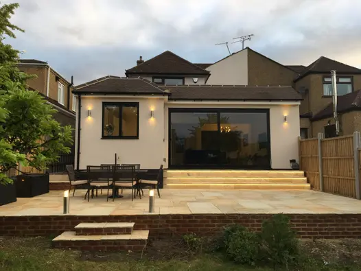 2 small steps rise from lawn to raised patio of Mint Indian sandstone paving at back of modern extension to semi-detached house.