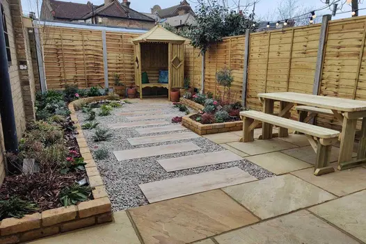 Small fenced garden with brick edged flower borders comapaved with mint Indian sandstone and gravel. Design by katerina Kantalis