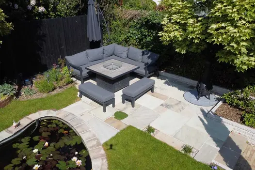 Garden  patio of Mint Indian sandstone paving with curved pond, borders with mature trees, and outdoor furniture.