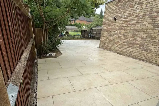Contemporary patio using Mint Porcelain Paving in a large-format layout beside a yellow-brick home.