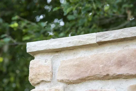 Close-up of a Mint Indian Sandstone coping stone next to brick wall, highlighting its rock-faced profile and hand-cut edges.