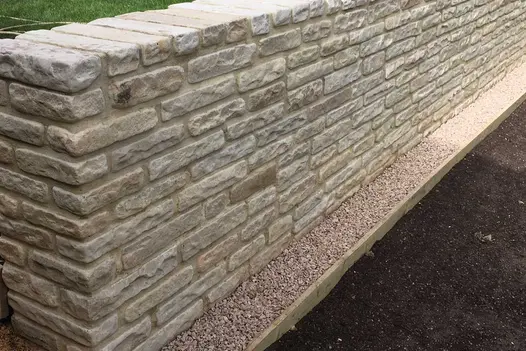 On either side of small raised bed of Mint sandstone walling 2 steps with matching brick risers descend from lawn to paving.