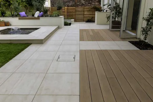 Mocha composite decking boards combined with Faro porcelain on patio between house and lawn, raised pond with fountain on left.