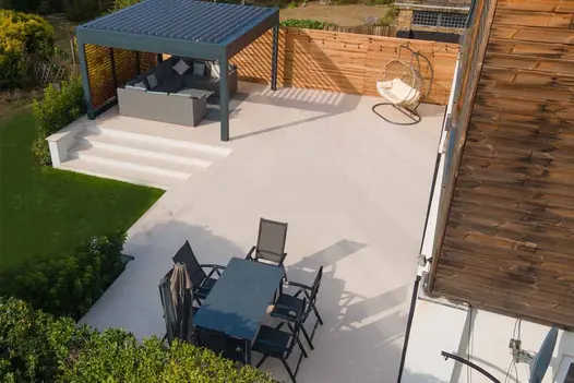 Contemporary garden with pergola-covered seating area on spacious Egyptian Light Porcelain Paving patio.