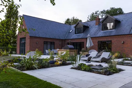 Sandy White Porcelain patio in front of converted barn, with inset rectangular flowerbeds, loungers and chairs. By Creative Roots.