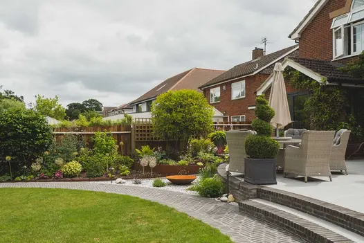 Path of Moderna clay pavers curves around lawn, with 2 steps up to patio with garden furniture. Built by Armstrong Landscapes.