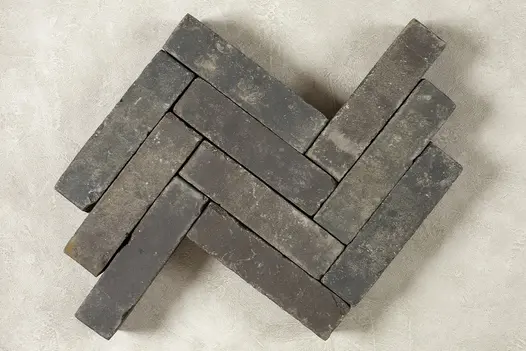 10 Moderna clay pavers laid in a herringbone pattern against a dark background, showing bricks’ tones of grey, white and beige