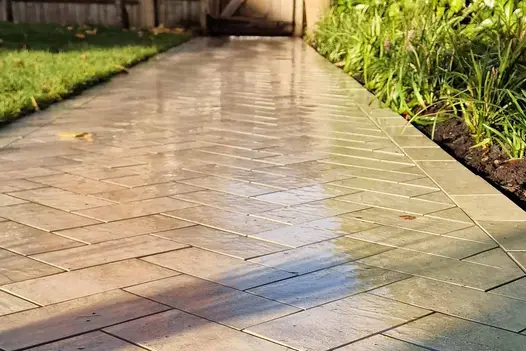 Low view along path of Cream porcelain paving setts laid herringbone between border and lawn, leading to wooden gate at end.